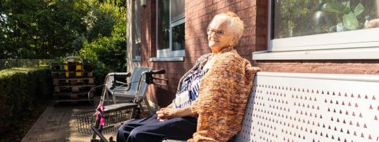 Older woman sitting at a bench at a house